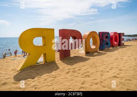 Iscrizione multicolore Yarovoe in lingua russa sulla sabbia gialla sullo sfondo del lago e dei turisti. Yarovoe nome della città di villeggiatura nel Foto Stock