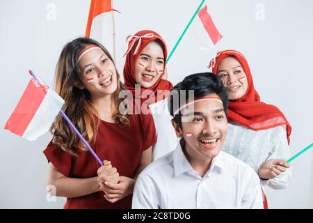 Gruppo di adolescenti che indossano attributi rosso e bianco con pompon e bandiere indonesiane con sfondo isolato Foto Stock