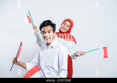 Un paio di adolescenti asiatici che indossano attributi rosso e bianco portano una piccola bandiera indonesiana con uno sfondo isolato Foto Stock