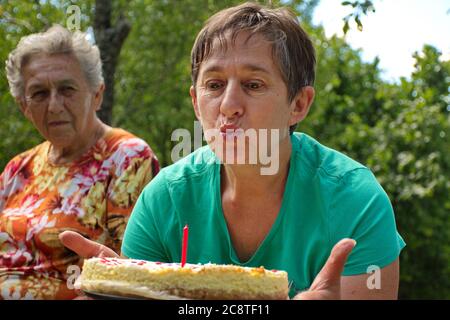 Ritratto di donna anziana che soffia candela sulla torta di compleanno Foto Stock