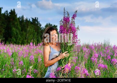 Bella donna in abito grigio si rilassa con mazzo di fiori sul prato di fireweed Foto Stock