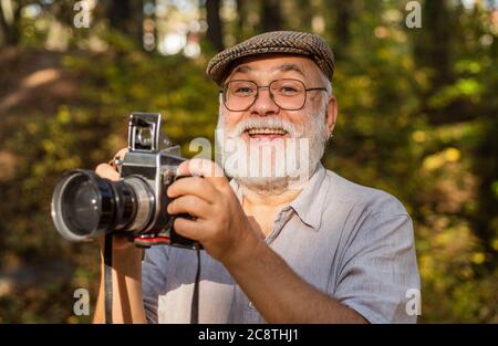 Fotocamera d'epoca. Noleggio fotografo vacanza. Ritratto di gioioso anziano uomo fare foto. Bel scatto. Retrò attrezzatura fotografica. Dire formaggio. La fotocamera reflex digitale è utilizzata per fotografare piante selvatiche. Foto Stock