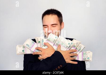 un esercito di soldi nelle mani di un giovane imprenditore. Rubli in confezioni. Milioni di rubli. Il vincitore della lotteria. Uomo d'affari gioioso. Il denaro è caduto Foto Stock