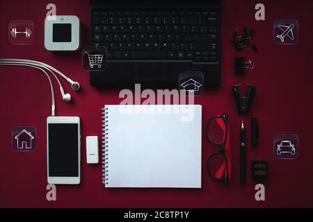 area di lavoro da scrivania per l'ufficio domestico con computer portatile, cuffie, smartphone con schermo nero su notebook e varie icone per risparmiare o spendere denaro Foto Stock