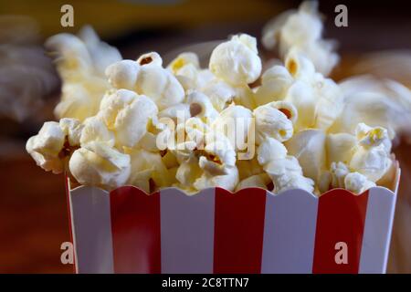 Popcorn che vola fuori dalla scatola di cartone. Secchio di popcorn a strisce rosse e bianche con popcorn volanti nel salotto, film o cinema Foto Stock