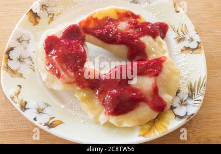 Vista dall'alto su un piatto con deserto ucraino tradizionale - vareniky farcito con ciliegia, aromatizzato con polvere di zucchero e lampone fresco e miele m Foto Stock
