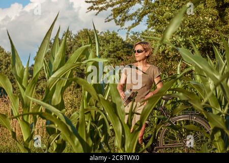 Una donna di mezza età si riposa in bicicletta nella natura nei sobborghi e gode della vista. Foto Stock