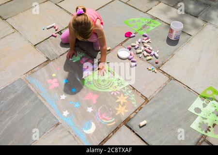 Una ragazza di cinque anni che amava herslef busily usando stencil di plastica a gesso forme su un pavimento di pietra flagstone. Foto Stock