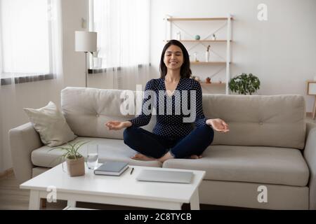 Felice ragazza asiatica sedersi sul divano pratica yoga a casa Foto Stock