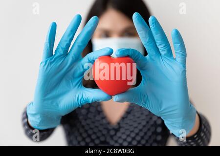 Primo piano di donna in abbigliamento protettivo mostra cuore letto Foto Stock