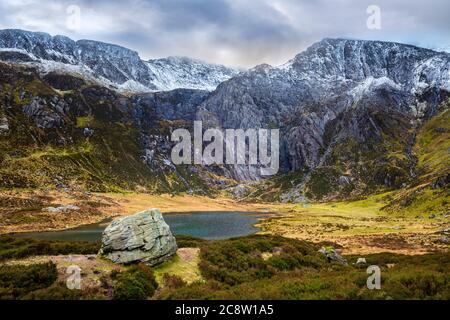 Un masso glaciale sopra Llyn Idwal con un Glyder Fawr coperto di neve sullo sfondo, Snowdonia National Park, Galles del Nord Foto Stock