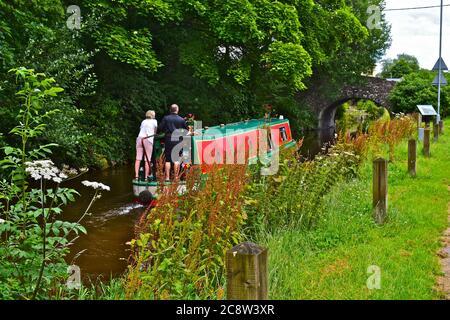 Una coppia che guida la loro barca di canale lungo il Monboccuthshire & Brecon Canal, alla periferia di Brecon. Vista dal percorso di traino. Foto Stock