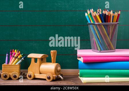 Concetto di ritorno a scuola, matite colorate, pastelli in cera e libri con treno giocattolo su sfondo vuoto lavagna Foto Stock