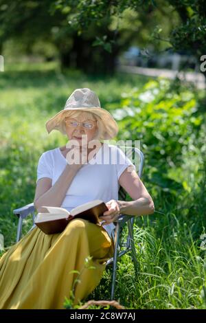 Donna anziana premurosa che legge un libro all'aperto Foto Stock