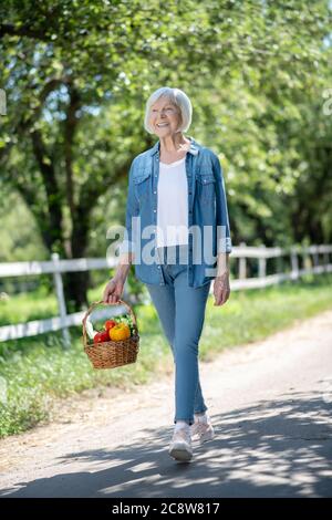 Donna rilassata che cammina con un cesto di verdure Foto Stock