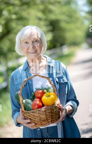 Donna sorridente che tiene un cesto di verdure biologiche fresche Foto Stock