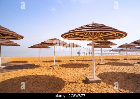 Ombrelloni di paglia dal sole sulla spiaggia sabbiosa del mare morto a Ein Bokek. Israele. Un bel posto per il riposo e il trattamento. Foto Stock