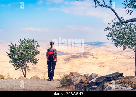 la donna backpacker si erge su una montagna e si affaccia sul deserto del Giordano vicino al mare morto. Il concetto di viaggio indipendente e avventura Foto Stock