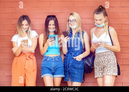 Ragazze giovani con maschere viso divertirsi utilizzando i telefoni cellulari all'aperto Foto Stock