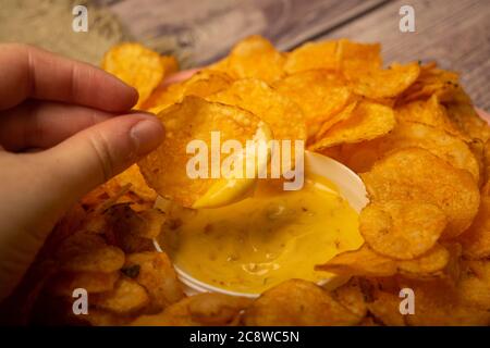 La ragazza prende un chip da un piatto rotondo con patatine e una pentola con salsa di formaggio al centro del piatto. Primo piano Foto Stock