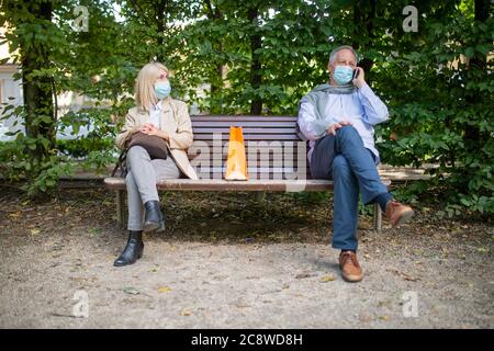 Concetto di allontanamento sociale e di separazione, prevenzione del coronavirus mentre si siede su una panchina in un parco Foto Stock