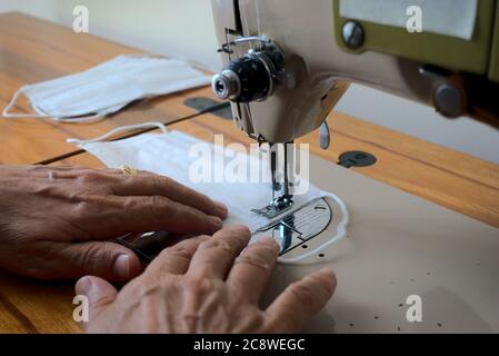 Primo piano sparato donna che indossa un anello di nozze fabbricazione maschera chirurgica utilizzando una macchina da cucire Foto Stock