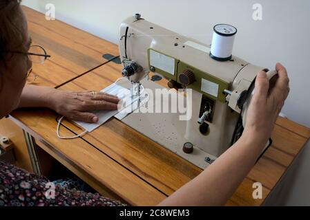 Primo piano shot donna che produce maschera chirurgica utilizzando una macchina da cucire - vista spalla Foto Stock