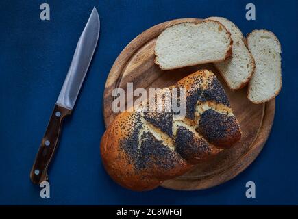 Vista dall'alto di un pane fresco bianco cosparso di papavero su un tagliere con fette tagliate e un coltello, sfondo blu Foto Stock