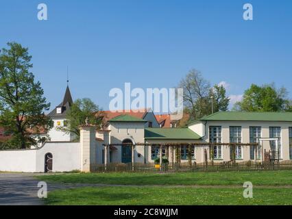 Repubblica Ceca, Praga, Dolni Pocernice, 21 aprile 2018: Vecchio municipio del villaggio con edifici circostanti, erba verde e alberi, cielo blu sfondo Foto Stock