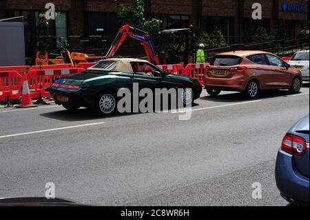 1998 Alfa Romeo bloccato in estate strada funziona con mini digger al lavoro Foto Stock