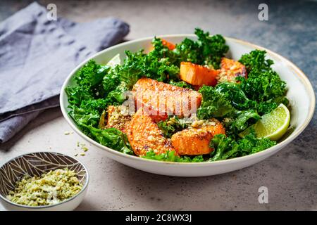 Insalata di patate dolci al forno con kale in una ciotola, sfondo scuro. Concetto di cibo vegano. Foto Stock