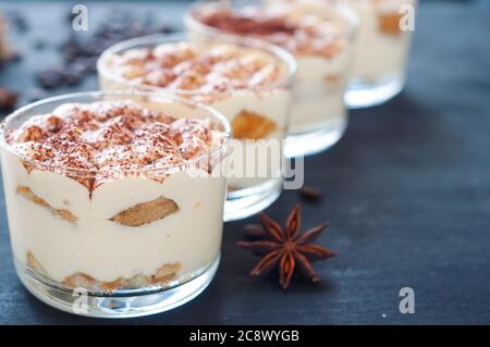 squisito tiramisù in bicchieri decorati con cacao in polvere su un sfondo scuro Foto Stock