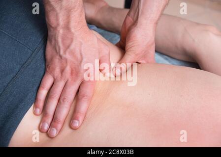 Il terapeuta fisico sta facendo un massaggio profondo su una parte inferiore della schiena di mans premendo duro con i pollici. Foto Stock