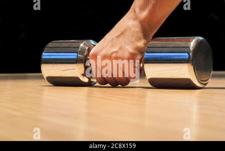 Primo piano della mano di un uomo mentre si raccoglie un manubri dal pavimento in legno Foto Stock