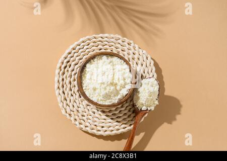 Polvere di collagene in ciotola e cucchiaio su fondo beige naturale con ombra. Vista dall'alto. Foto Stock