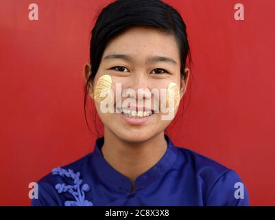 Giovane donna birmana con la forma a foglia tradizionale thanaka faccia cosmetic sulle sue guance sorride per la macchina fotografica. Foto Stock