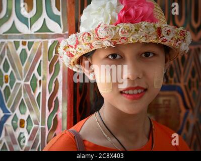 Bella ragazza birmana con naturale thanaka faccia cosmetic sulle sue guance pone per la macchina fotografica con un cappello di paglia elegante al buddista su Taung Pagoda. Foto Stock