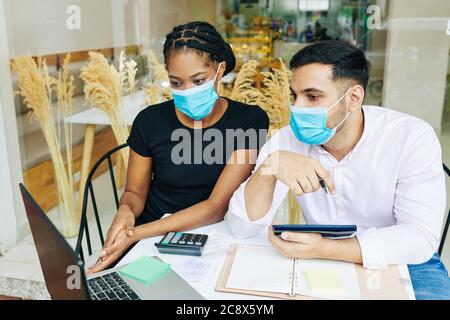 Seri giovani proprietari di panetteria in maschere mediche che discutono i rapporti finanziari dopo la bocca del lavoro durante la pandemia Foto Stock