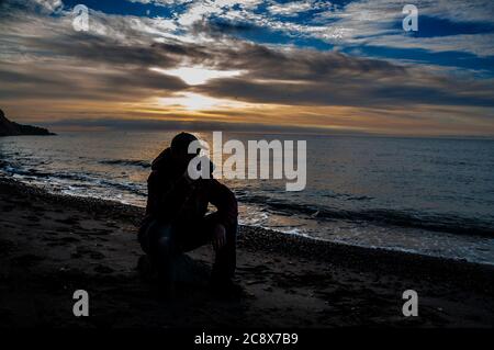 Tazza di tè del mattino. Uomo seduto su una roccia e bere tè all'alba su una spiaggia di mare. Foto Stock