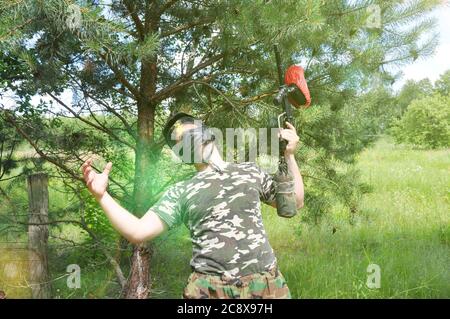 il giocatore di paintball in uniforme camouflage e maschera protettiva è stato ucciso dal nemico in testa. Foto Stock