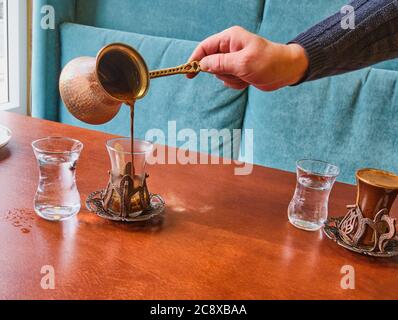 Una mano barista maschile che versa caffè turco fresco da un turk in un bel bicchiere di stile orientale. Foto Stock