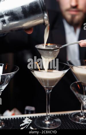 mani di un barman che tiene un agitatore che versa una bevanda in un bicchiere martini Foto Stock