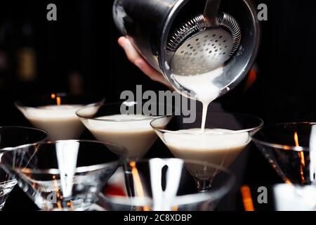 mani di un barman che tiene un agitatore che versa una bevanda in un bicchiere martini Foto Stock