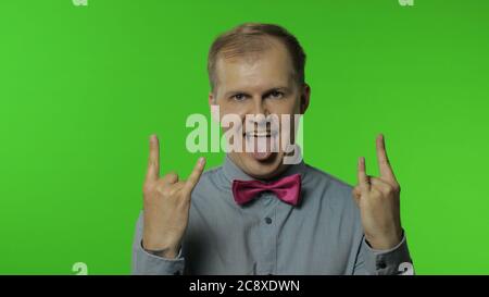 Spensierato felice uomo felice che dimostra lingua fuori e rock e roll mano gesto, punk segno, gridare eccitato da vincere, pazzo circa il successo. Ritratto di ragazzo che posa su sfondo chiave chroma Foto Stock