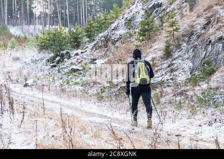 Ekaterinburg, Russia - 9 novembre 2019: Un uomo con uno zaino con bastoni scandinavi in una tuta nera sportiva e sneakers va in salita attraverso Foto Stock