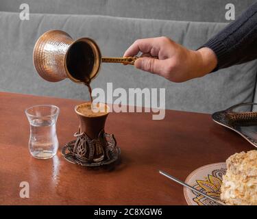 In un caffè, il caffè turco aromatico forte con la schiuma viene versato dalla turca in un bel bicchiere. Foto Stock