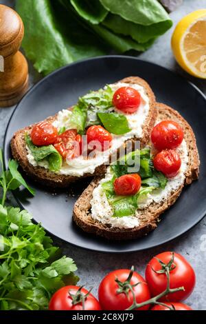 Bruschetta con ricotta e pomodori su piatto nero. Gourmet panino italiano aperto Foto Stock