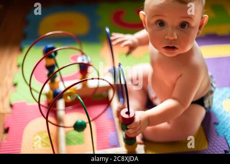 Bel bambino ragazzo in poppa che gioca con i suoi giocattoli educativi in legno fatti di colori e forme e guardando la macchina fotografica con l'espressione divertente e sorpresa. Foto Stock