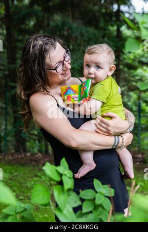 Ritratto esterno in luce naturale. La mummia sta tenendo suo figlio tra le braccia, il bambino sta guardando la macchina fotografica mentre la mummia lo guarda con occhi amorevoli. Foto Stock