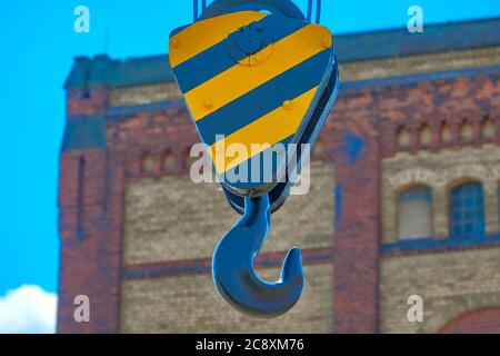 Gancio in ferro per impieghi pesanti con fissaggio nero e giallo davanti a una facciata intenzionalmente sfocata di un edificio industriale Foto Stock